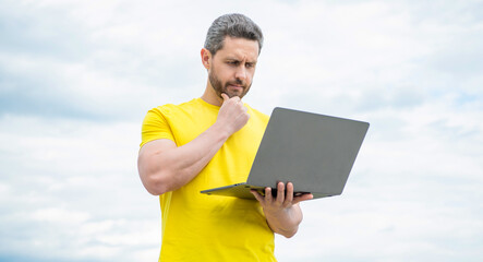 pondering man working online on laptop on sky background