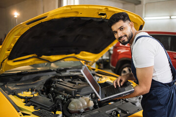 Wall Mural - Mechanic man mechanic manager worker using a laptop computer checking car in workshop at auto car repair service center. Engineer young man looking at inspection vehicle details under car hood