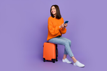 Sticker - Full size photo of cute young woman hold device wait taxi service wear trendy orange knitwear garment isolated on violet color background