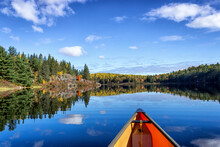 Trees And Clouds Reflect On The Calm Blue Water During A Canoe Trip In Algonquin Provincial Park. 