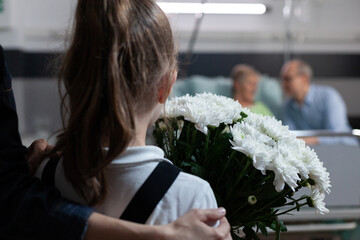 Wall Mural - Unrecognizable little girl holding flowers bouquet arriving at nursing home, visiting sick grandmother. Toddler seeing elderly lady in hospital observation room with flower arrangement as gift.