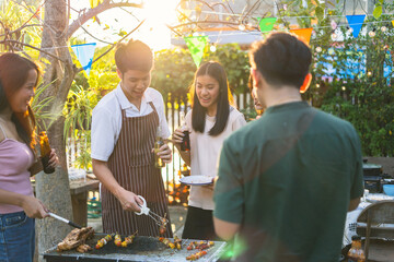 Wall Mural - A group of Asian friends clinks a wine bottle during a party barbecue.