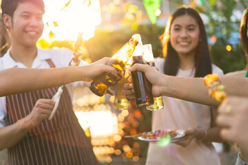 Wall Mural - A group of Asian friends clinks a wine bottle during a party barbecue.