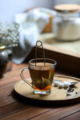 Poster - Cup of freshly brewed tea with snap infuser and sugar cubes on wooden table indoors