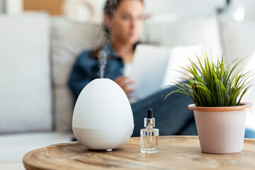 shot of essential oil aroma diffuser humidifier diffusing water articles in the air while woman read