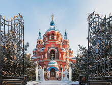 Winter Irkutsk. Cathedral Of Kazan Icon Of Mother Of God During Christmas Holidays. View Of Churchyard With Ice Sculptures Of Saints From Entrance With Wrought Iron Gates. Translation: Merry Christmas