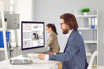 People at work in modern office. Busy employees working on computers. Male and female workers sitting at desks with desktop and laptop PCs, working with data, using different business software