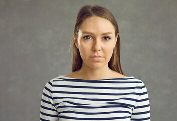 Headshot of good-looking lady in her 20s or 30s in striped top. Studio portrait of young woman in her twenties or thirties looking at camera with serious unemotional face expression