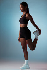 Fitness, exercise and black woman stretching her leg in studio before sports training or workout. Healthy, athlete and slim African model doing warm up in sportswear while isolated by blue background