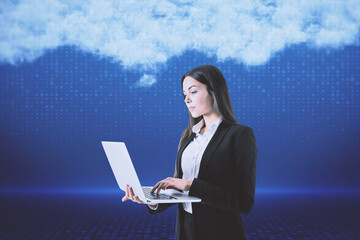 Poster - Attractive young european woman with laptop standing on blurry digital blue background with abstract cloud. Cloud computing, big data and digital transformation concept.