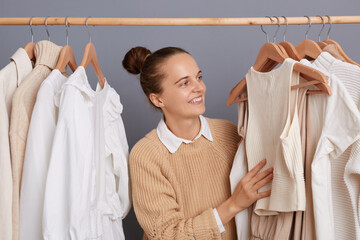 Wall Mural - Portrait of attractive smiling positive Caucasian woman standing near clothes hang on shelf, choosing shirt from a new collection, smiling, enjoying shopping.