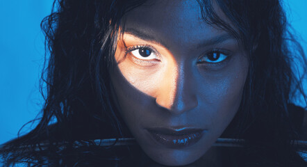 Poster - Beauty, cosmetics and portrait of a model with a light reflection on her face in the studio. Spotlight, skincare and young woman from Puerto Rico with natural skin isolated by a blue background.