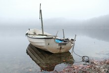 White Wooden Boat On Shore Of Lake In Calm Misty Day. 