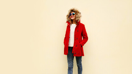 Canvas Print - Stylish smiling young woman wearing red coat jacket with fur hood walking looking away on background, blank copy space for advertising text