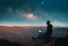 Mature Latin Man Sitting On Top Of A Hill Above A City With Laptop Looking At The Milky Way