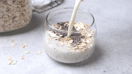cooking overnight oats with chia seeds in glass jar. the process of preparing breakfast. pouring mil