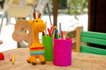 Zone for children entertainment in cafe. On outdoor terrace, there are colorful pencils, a toy giraffe, and a chair in glass on table.