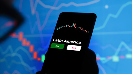 An investor's analyzing the Latin America etf fund on screen. A phone shows the ETF's prices south america to invest