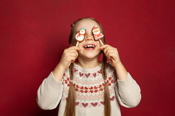 Funny joyful child girl having fun with Santa Claus and Snowman gingerbreads on red studio wall banner background