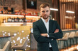 © standret - Confident man in black suit is standing in the bar with arms crossed