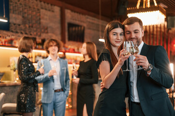 Wall Mural - Man with woman is posing. Group of people in beautiful elegant clothes are celebrating New Year indoors together