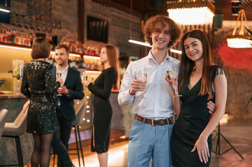 Wall Mural - Man with woman is standing and posing. Group of people in beautiful elegant clothes are celebrating New Year indoors together