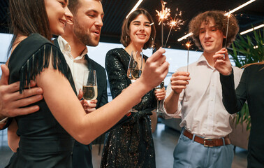 Wall Mural - Amazing sparklers. Group of people in beautiful elegant clothes are celebrating New Year indoors together