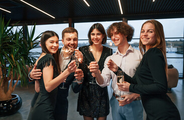 Wall Mural - Sparklers light. Group of people in beautiful elegant clothes are celebrating New Year indoors together