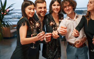 Wall Mural - Sparklers light. Group of people in beautiful elegant clothes are celebrating New Year indoors together