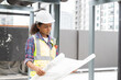 © amorn - Portrait of female engineer working with construction building blueprint at sewer pipes area at construction site on rooftop of building