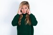 Serious concentrated beautiful caucasian teen girl wearing green knitted sweater keeps fingers on temples, tries to ease tension, gather with thoughts and remember important information for exam