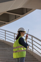 Wall Mural - female engineer with a walkie-talkie at the construction site gives instructions. European successful female technologist or fire safety engineer works. foreman in a white helmet and protective yellow