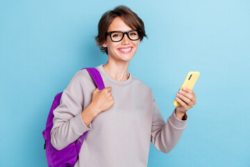 Poster - Photo of cheerful positive pretty lady hold bag telephone modern device gadget stand empty space isolated on blue color background