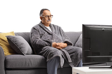 Mature man wearing a bathrobe, sitting on a gray sofa and watchin tv