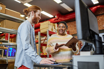 Portrait of two young people working in print shop and using computer, copy space