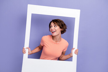 Sticker - Photo of cheerful pretty lady wear stylish clothes interested look empty space hand hold paper frame isolated on purple color background