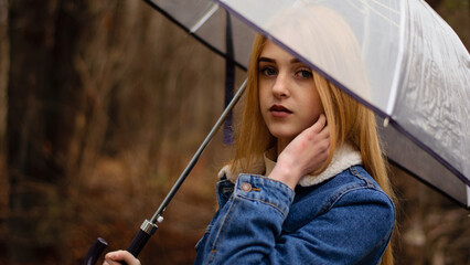 young girl with umbrella walking in at beautifu autumn park. modern girl in casual clothes walks through the city park. Seasonal style, autumn beauty. autumn season, in a blue jacket, in autumn leaves