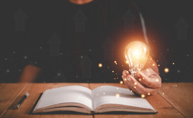 Wall Mural - Hand holding light bulb on the open book, Thinking and creative concept, Knowledge and searching for new ideas, Education, Innovations, self-learning, Inspiring from read.