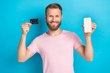 Wall Mural - Photo of positive pretty guy dressed pink t-shirt rising credit card modern gadget empty space isolated blue color background