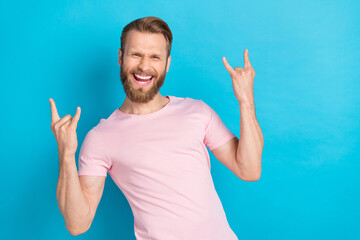 Poster - Photo of sweet funky young guy dressed pink t-shirt showing rock roll gestures empty space isolated blue color background