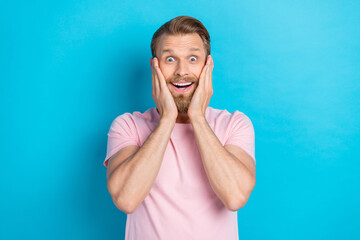 Poster - Photo of excited funky young guy dressed pink t-shirt rising arms cheeks smiling isolated blue color background