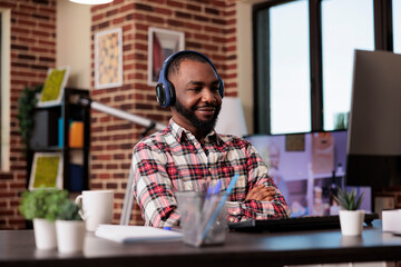 Poster - African american man using headphones and working remotely on computer at home desk. Listening to music or podcast show online on social media internet, attending class lesson webinar.