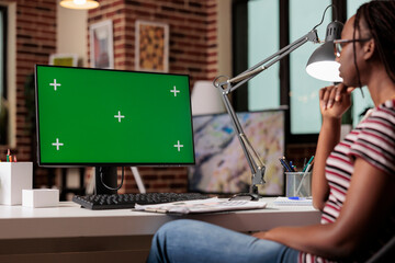 Poster - African american remote worker looking at computer with green screen, pc with chroma key monitor mock up. Freelancer working home office with modern interior, sitting at workplace desk