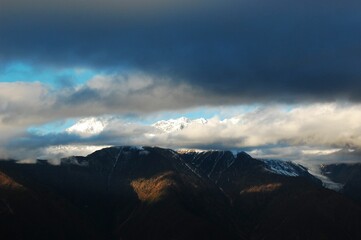 Sticker - Wide shot of snow-covered mountains with large clouds covering their full view.