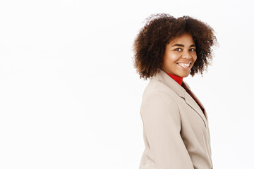 Portrait of smiling african american businesswoman, company worker in suit, standing half turned, looking professional, standing over white background