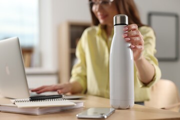 Wall Mural - Woman holding thermos bottle at workplace, focus on container. Space for text