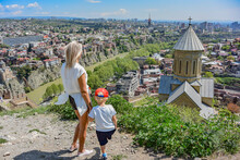 Tbilisi, Georgia-April 28, 2019: A Young Girl With A Child On The Background Of A Beautiful Bird's-eye View Of The Central Part Of Tbilisi And The Church Of St. Nicholas The Wonderworker.