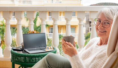 Wall Mural - Portrait of smiling senior woman having relax at home balcony with a coffee cup looking at camera. Adult attractive female people enjoying quiet lifestyle outdoor