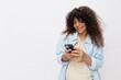 © SHOTPRIME STUDIO - A pregnant woman smile looks at the phone in her hands, online communication and correspondence with the doctor pregnancy management, on a white isolated background in a T-shirt with a blue shirt