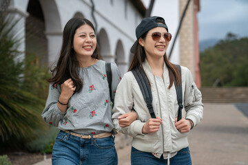 Wall Mural - closeup portrait of two asian Taiwanese young women backpackers having fun touring around old mission santa Barbara in usa. they stand arm in arm and look into space with smiling face